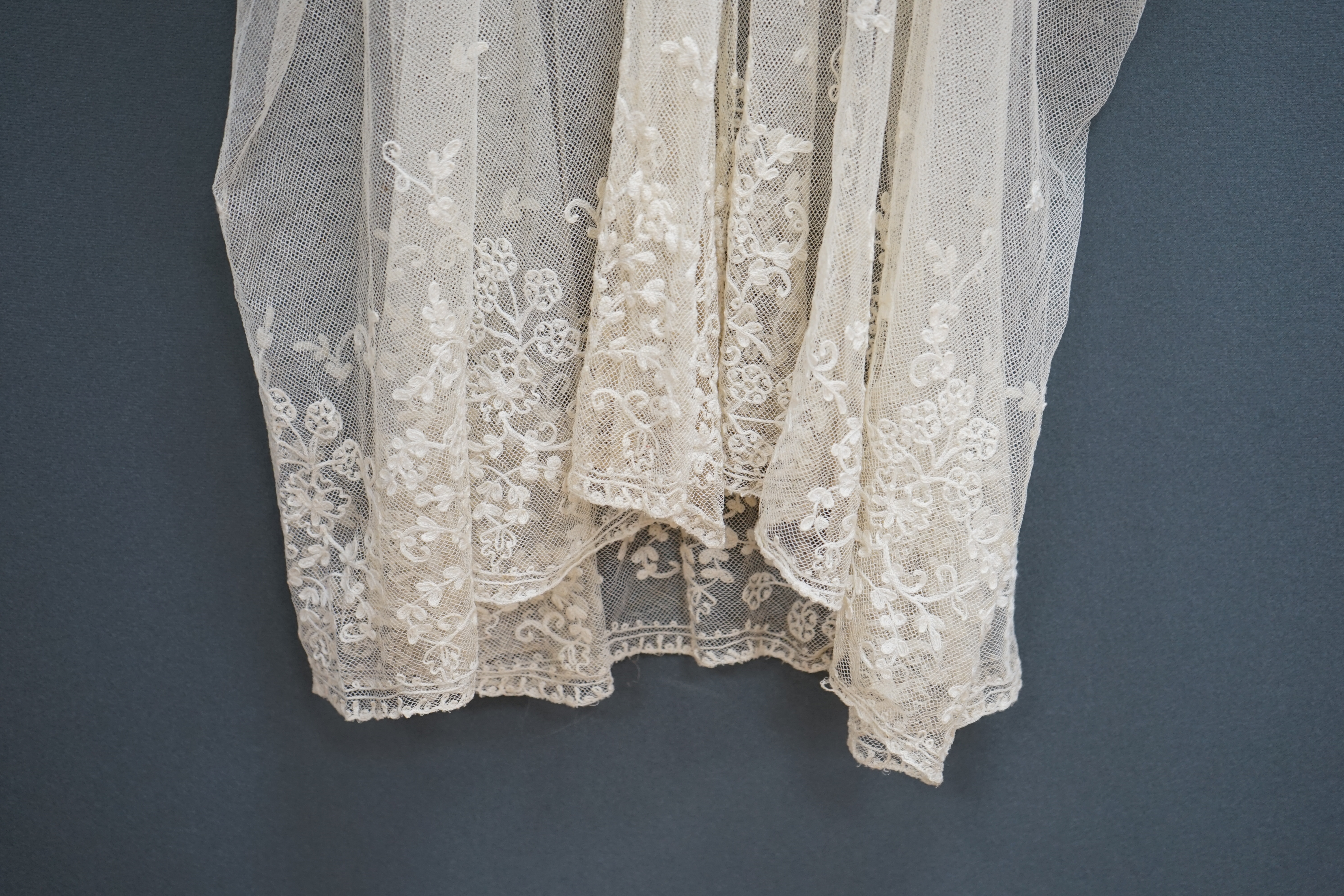 A 1920's cream net and needle run, lace wedding dress, together with a small silk net veil, and lace boudoir cap, the dress worked with a deep needle run bodice and skirt edge, with all over sprig motifs, designed with a